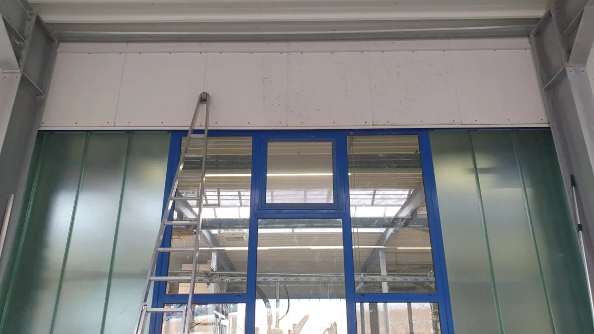 Reinigung einer großen Glas- und Metallfront in einer Betriebshalle