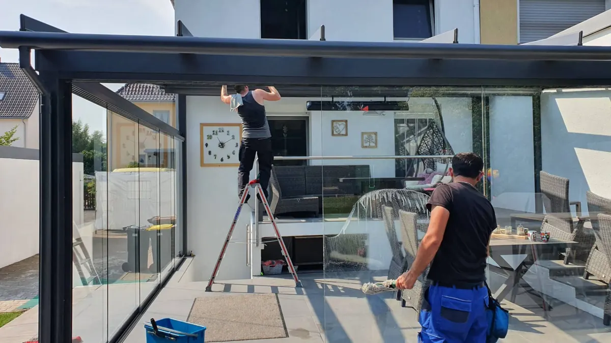Zwei Mitarbeiter reinigen einen Wintergarten mit Leiter und Teleskopstange