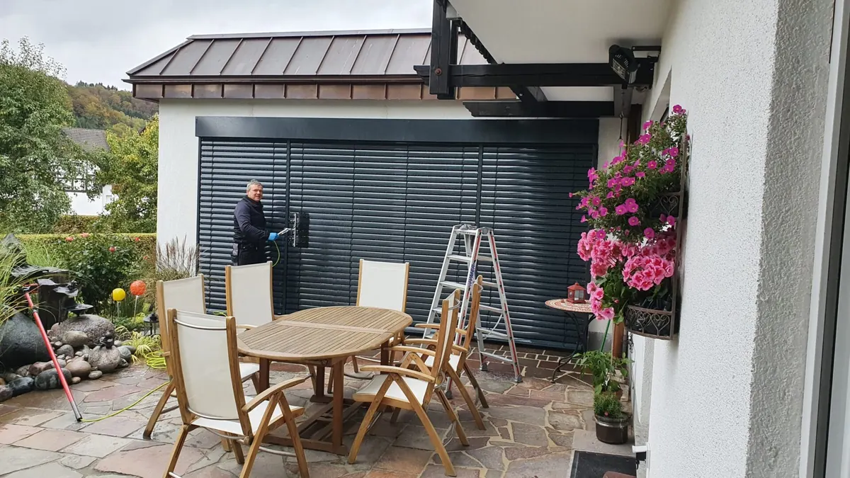 Mitarbeiter reinigt eine Außenjalousie an einer Terrasse