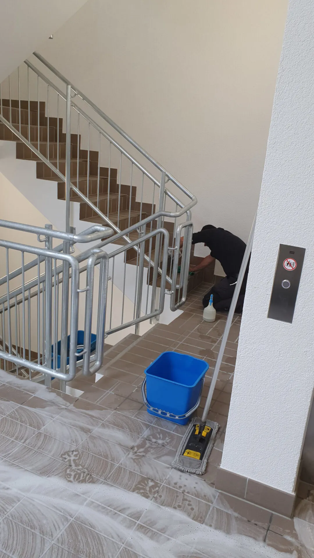 Mitarbeiter reinigt ein Treppenhaus mit Bodenpad und Eimer