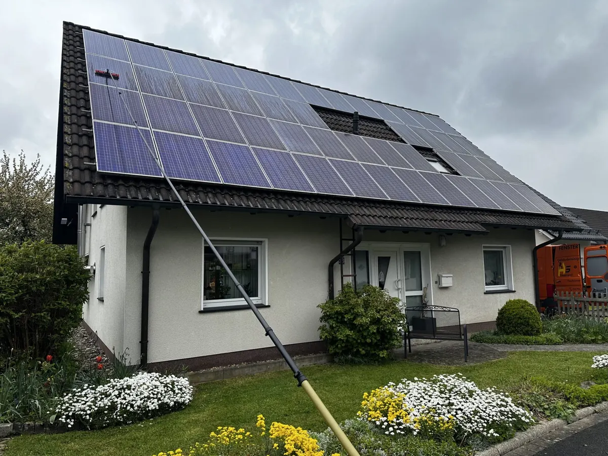 Photovoltaikanlage auf einem Einfamilienhaus wird vom Garten aus mit einer wasserführenden Stange gereinigt