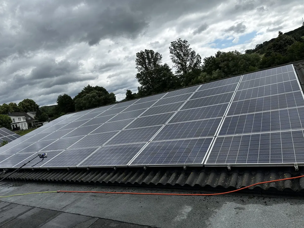 Große Photovoltaikanlage auf einem Hallendach, im Hintergrund bewaldete Sauerland-Hügel