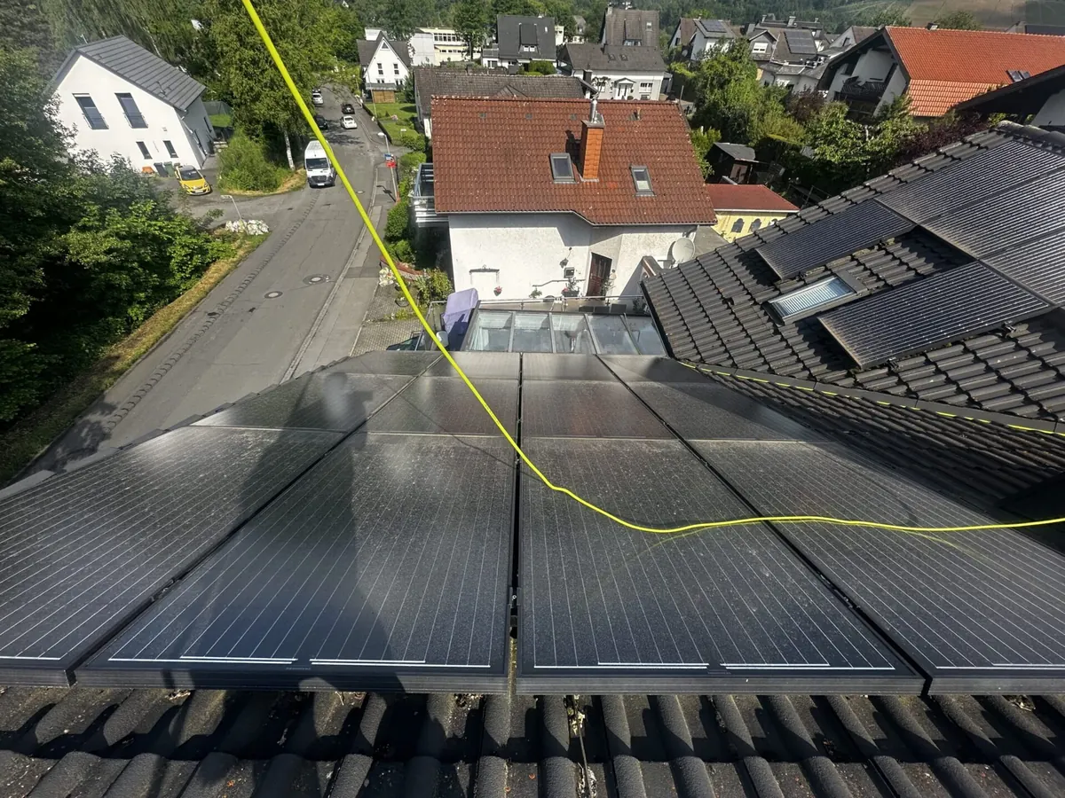 Photovoltaikmodule auf einem Hausdach werden mit Stange und wasserführendem Schlauch gereinigt